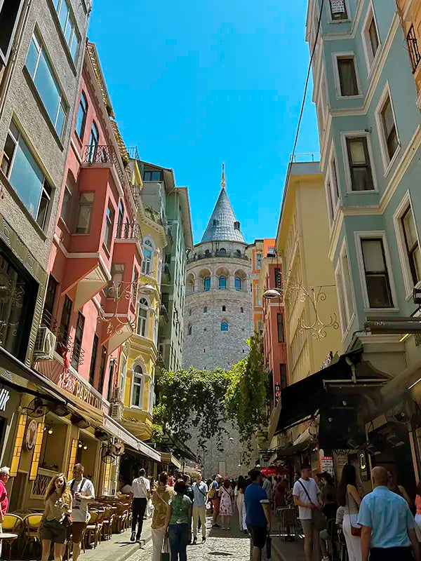 Historical tower view from the street, colorful buildings on the street and people are walking on the street