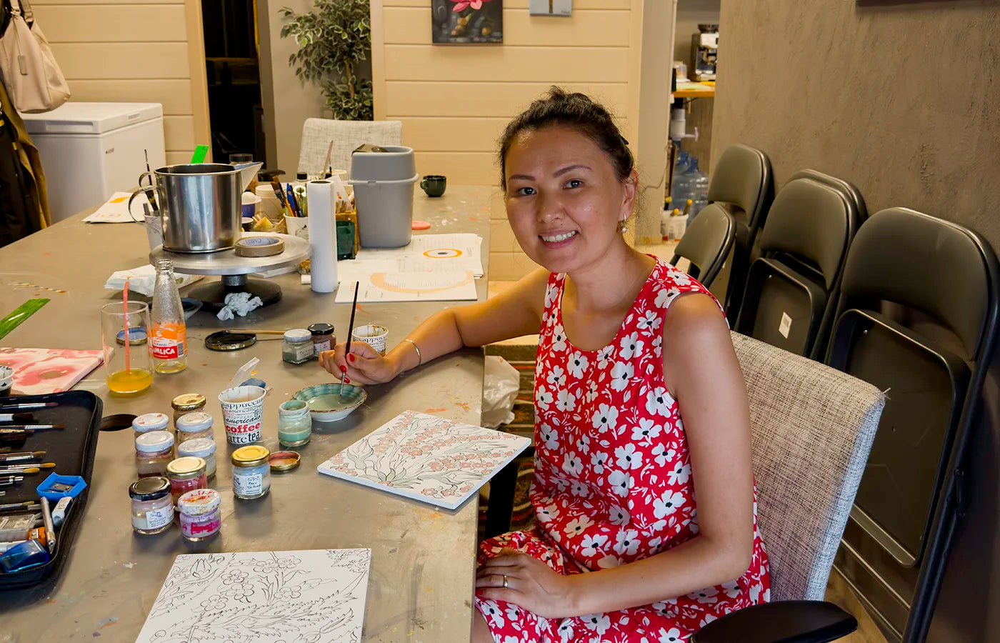 Woman in red floral dress painting floral design on square flat ceramics